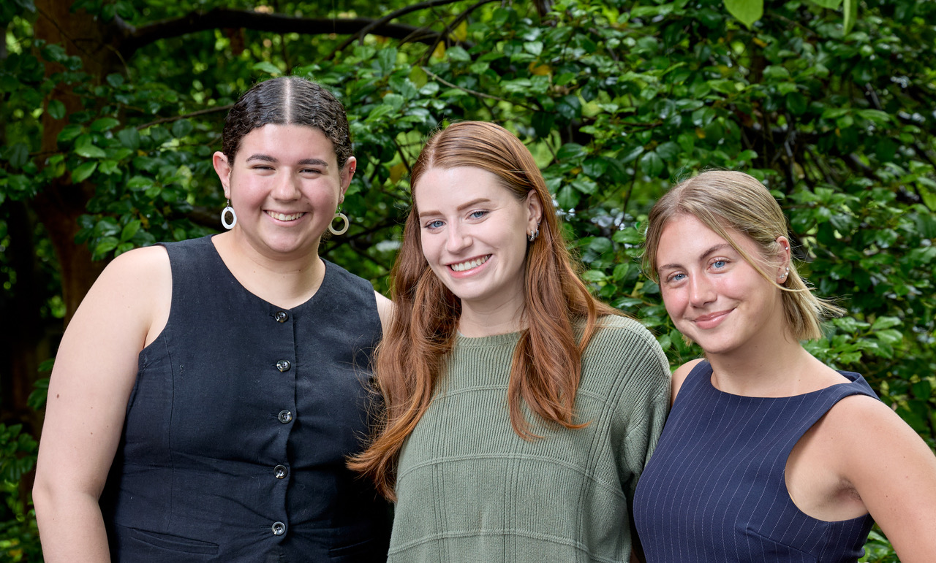three students smiling with greenery in background